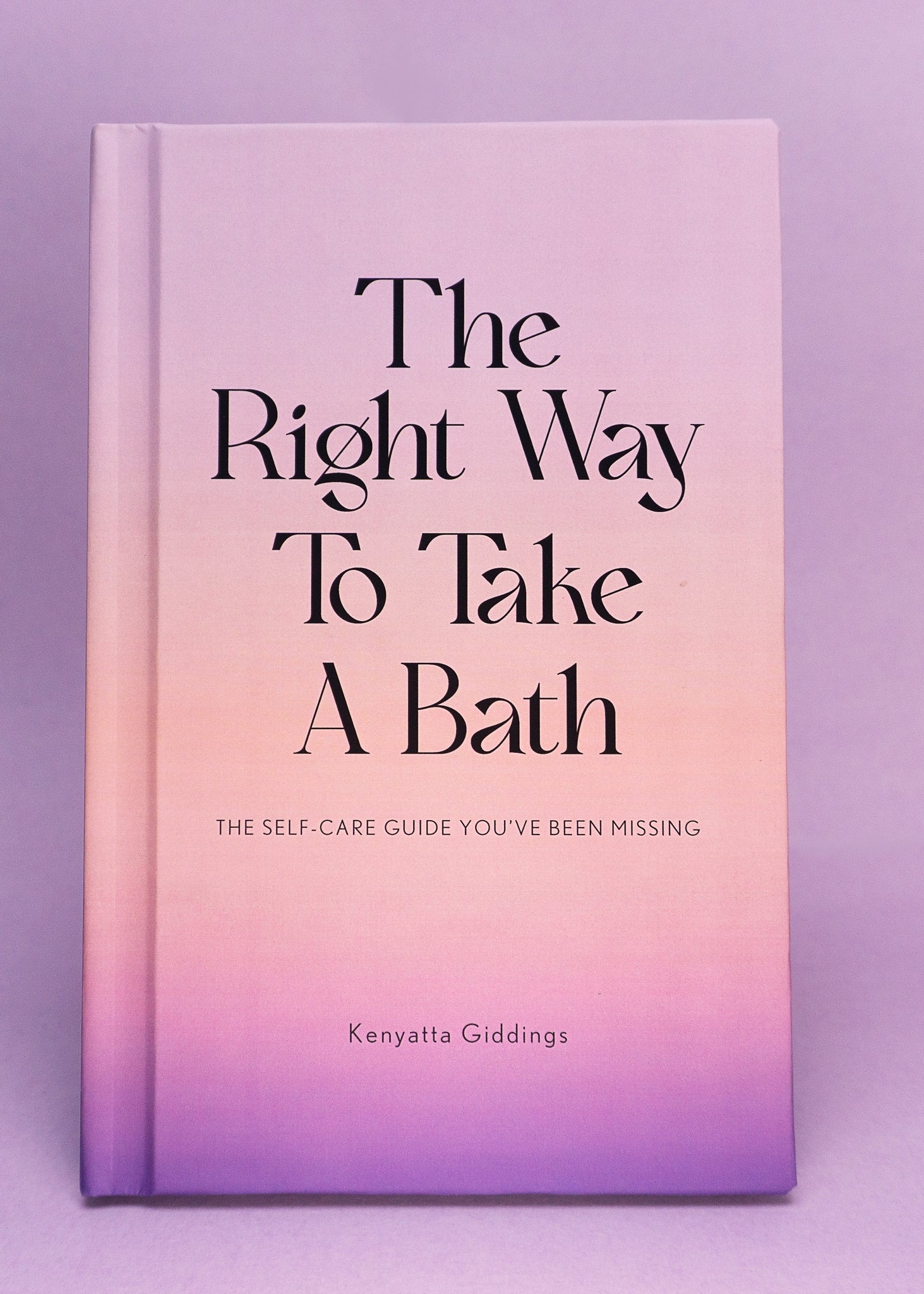 The Right Way To Take A Bath hardcover book with a soft touch matte pastel cover against a light purple background. The Right Way To Take A Bath is a self-care guide that captures bubble bath tips in a decor-friendly book that makes the perfect spa gift.