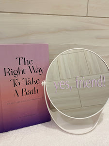 Positive affirmation pink mirror decal without air bubbles on white bathroom mirror next to The Right Way To Take A Bath book. Decal for daily positive affirmation. Mirror affirmation decal placed on modern white mirror for bathroom. White mirror for bathroom has a tray for skincare products.